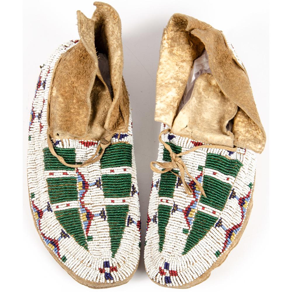 Cheyenne Beaded Buffalo Hide Miccasins: thread and sinew-sewn on buffalo hide, beaded geometric design in colors of white, red white-heart, greasy yellow, periwinkle, navy, and translucent green, length 9.5 in. late 19th century
