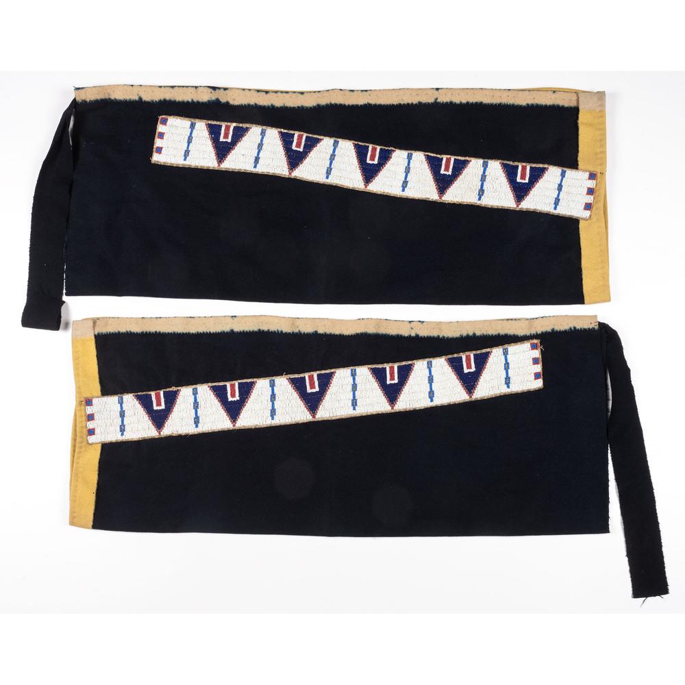 Cheyenne Beaded Wool Leggings: beaded hide strips thread and sinew-sewn using colors of red white-heart, marcasite, dark blue, medium blue, and white; strips are placed on a blue wool trade cloth, overall length 33 in. x width 13 i