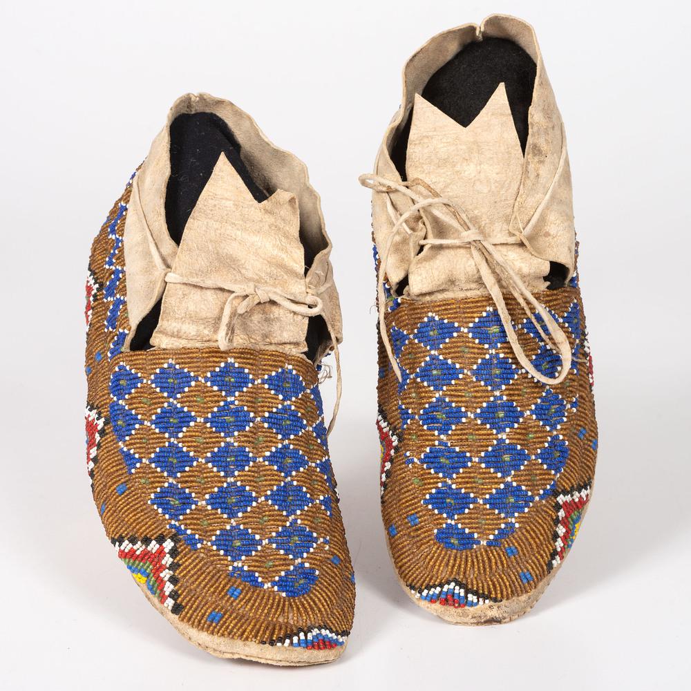 Sioux Beaded Hide Moccasins: sinew-sewn and beaded using a unique color palette of dark blue, translucent green, apple red white-heart, and white against an amber ground, length 10.5 in. ca 1900