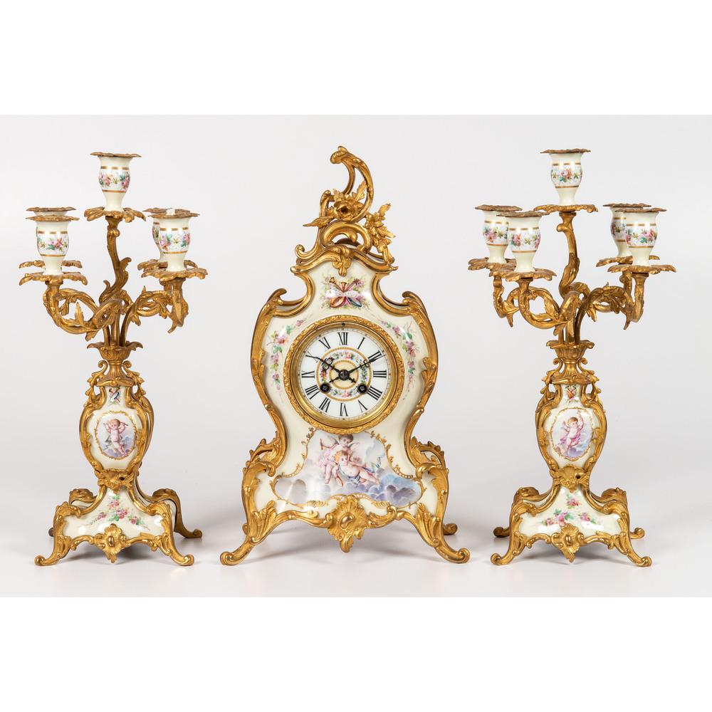 A Louis XV-style Gilt Bronze and Porcelain Garniture: French, Early 20th Century three-piece set with clock and matching five-light candelabra. Height of clock 16 1/2 x width 9 1/4 inches.