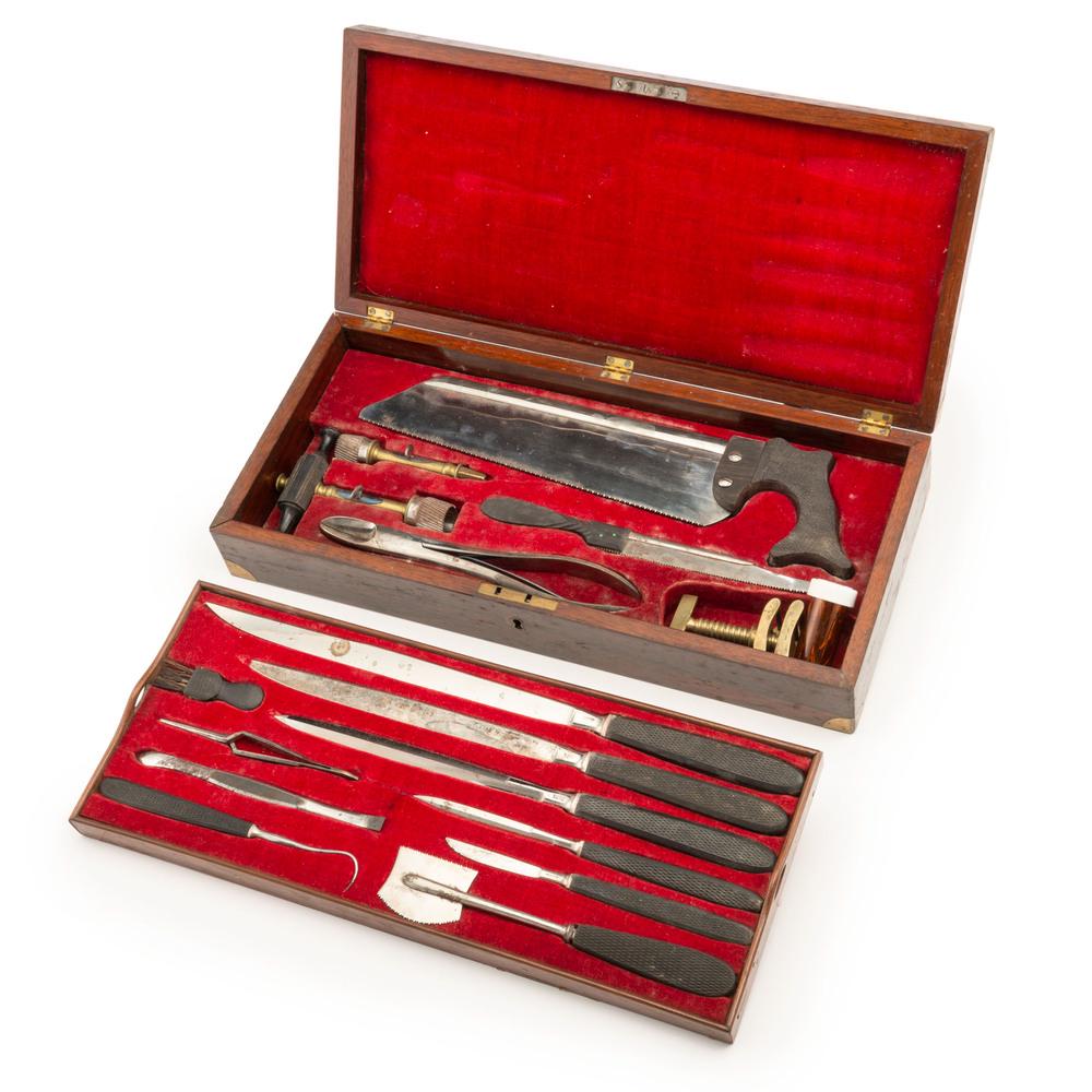 Surgical Amputation Kit with Instruments by Gemrig,: Wooden case, 16.5 x 7.5 x 3.125 in., with brass fittings, red velvet lining, and removable tray. Kit includes trephines with handle, tourniquet, scalpels, amputation saw, Hey saw, forceps, tenaculum, 
