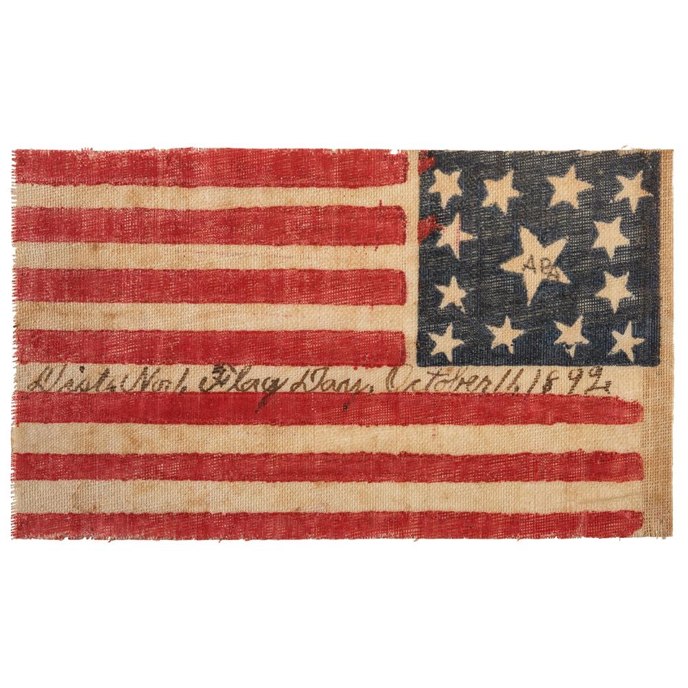 13-Star Columbus Day Flag: Printed flag on glazed muslin, 3.5 x 5.75 in. Wreath pattern with central star, flanked by star in each corner. Initials “APA” handwritten within central star. Ink inscription: "Dist. No 1. Flag D