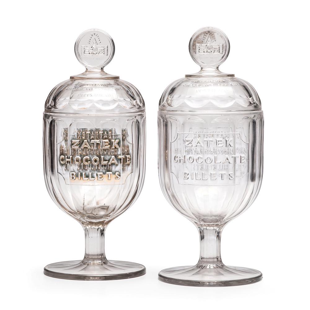 Two Zatek Chocolate Billets Molded Glass Display Jars: Pittsburgh, Pennsylvania, circa 1907 one retains remnants of a gilt finish. Height of taller 16 3/4 inches.