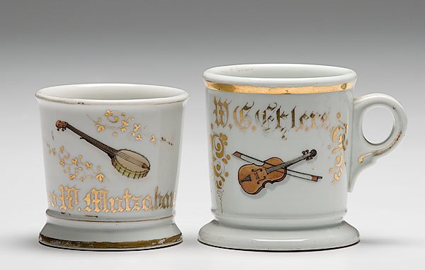 Two Musician's Occupational Shaving Mugs, : Two Musician's Occupational Shaving Mugs, porcelain mugs with polychrome painted scenes of musical instruments. First is a banjo. Gilt name Geo. W. Mutzabaugh. Second is a violin. Gilt name W.G. Ehl