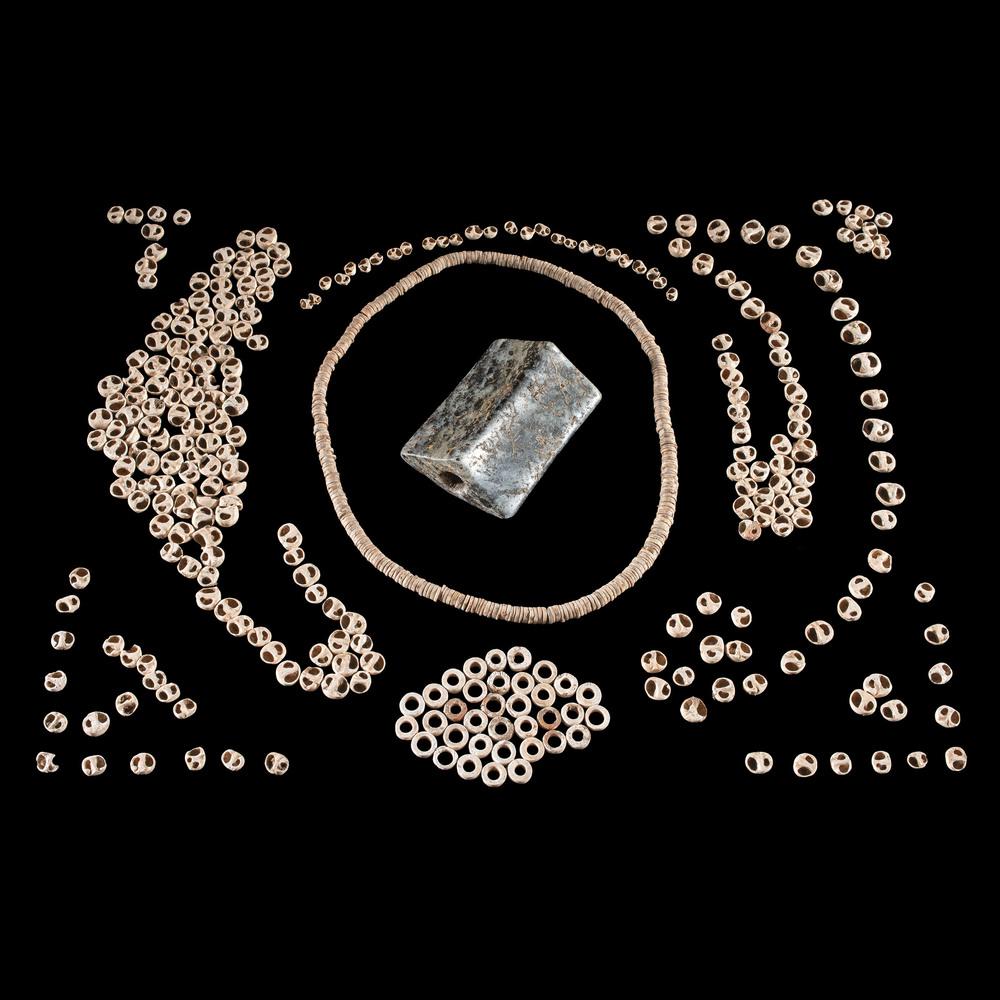 A Quartz Saddle Bannerstone AND Shell Beads, Largest: Middle - Late Archaic Period, 8000-1000 B.C. Pond River, Kentucky [all] Bannerstone is broken in half and expertly restored. frame, longest 2-5/8 in. Collection History: Gerber Collection Number: A