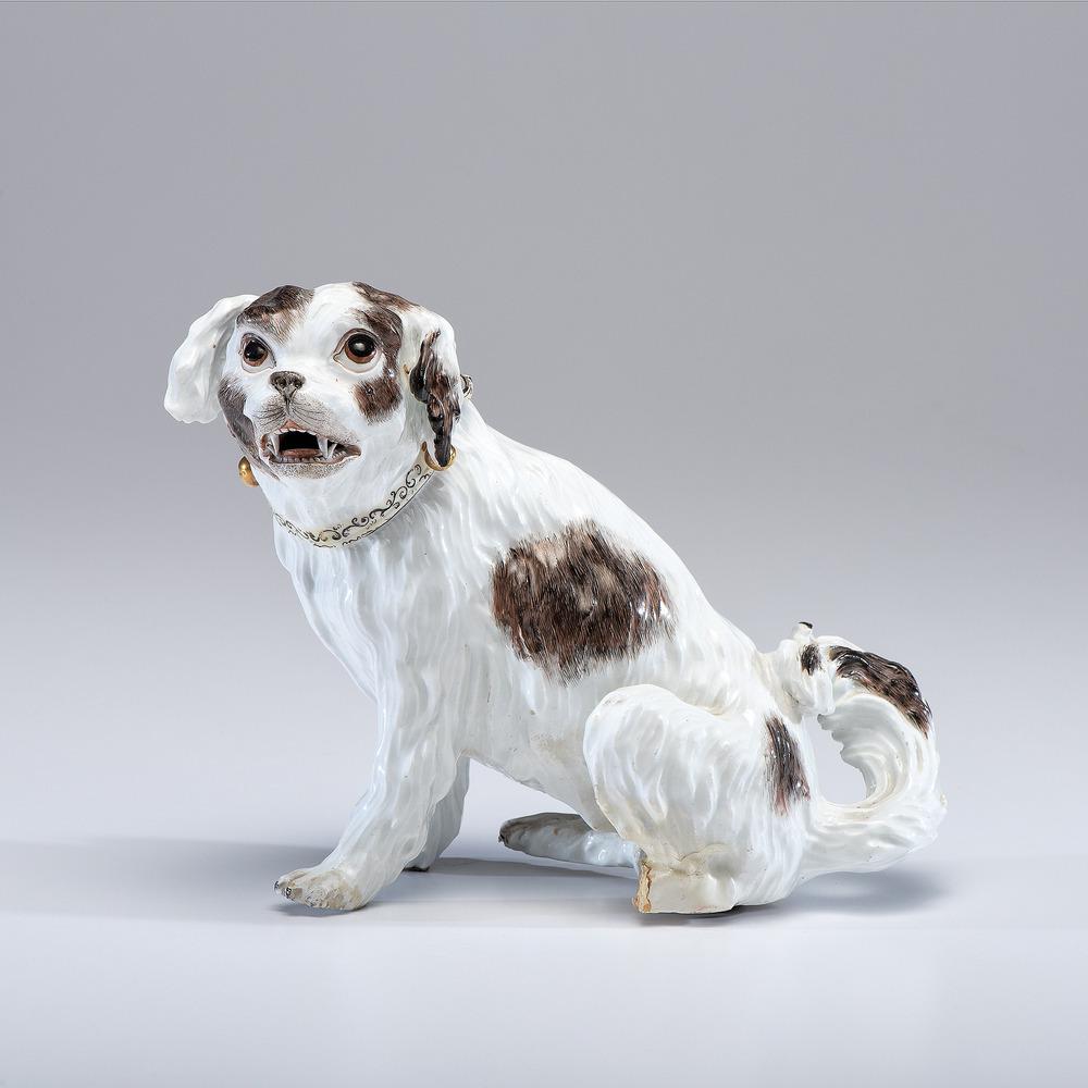 A Meissen Porcelain Dog: German, 19th Century. wearing scrollwork collar with three gilded bells. with blue underglaze mark near tail. Height 7 1/2 inches. Provenance: Property of Anne Romanoff Ilyinsky