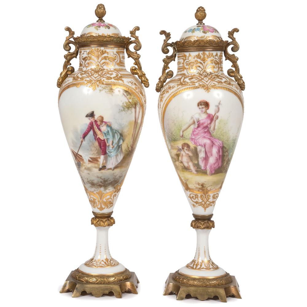A Pair of Sevres-style Lidded Urns in White and Gilt: French, 19th/20th Century with hand-painted reserves and ormolu mounts. one signed Guerard, the other signed Huchet on front. Height 14 inches. Provenance: Property from the Actors Theatre of Louisv