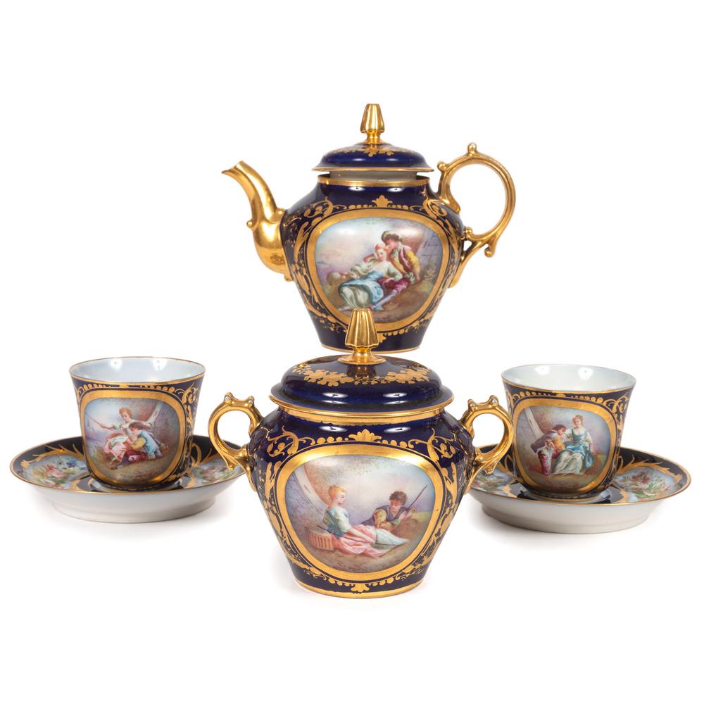 A Sevres-style Four-Piece Tea Set in Cobalt: French 19th/20th Century includes a teapot, lidded sugar and two cups and saucers. each with reserves of florals and courtship scenes. each marked with interlocking Ls. Height of teapot 5 3/4 inch