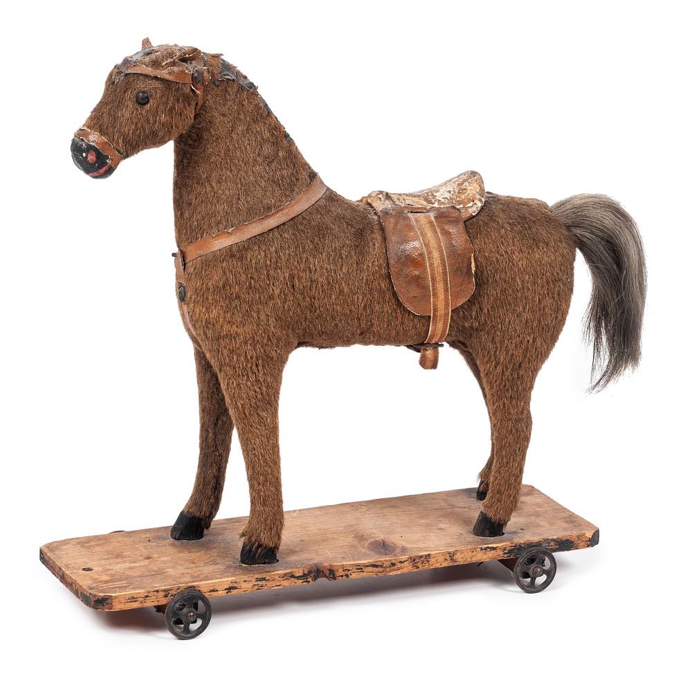 A Horse Pull Toy: A Horse Pull Toy having a fur covered body, glass eyes and leather saddle, on a wooden platform. Height 14 x length 13 1/2 x depth 4 inches. Property of the late Karen Tosterud, Bellaire, Michigan We 