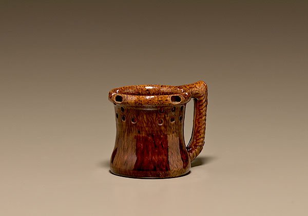 George Ohr Puzzle Mug, : George Ohr Puzzle Mug, American, Biloxi, Mississippi, ca 1900. Interior and exterior decorated with a mottled brown glaze, with molded rope handle. Three drinking holes along the rim and 16 holes ar