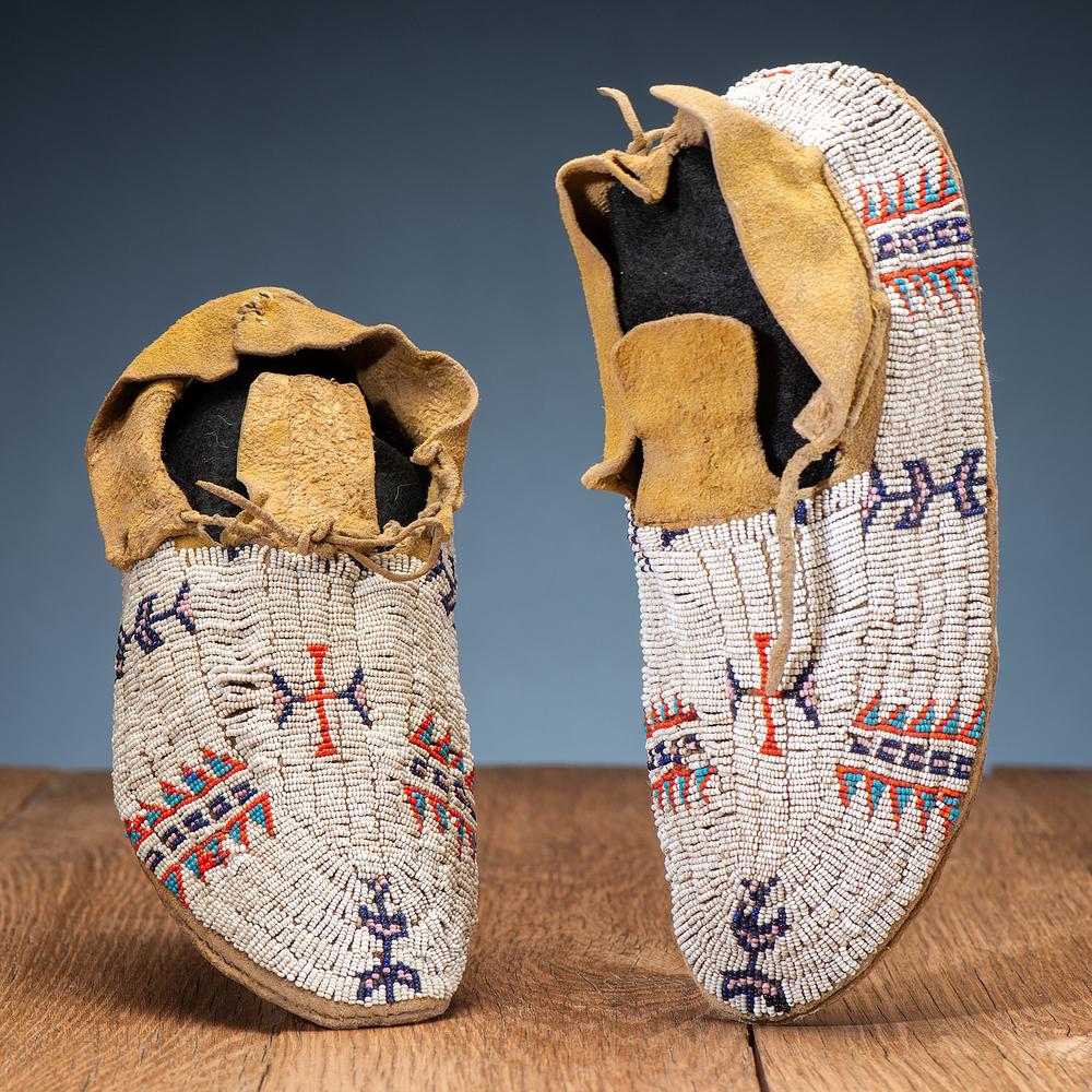 Cheyenne Beaded Hide Moccasins: thread and sinew-sewn; beaded on thick hide in colors of apple red white-heart, light blue, cobalt, white, and pink; hided coated with yellow pigment length 10.5 in. early 20th century