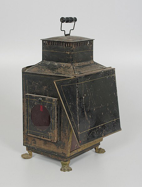 Tin Miner's Lantern : Tin Miner's Lantern American. A tin miner's oil lantern with hinged door and a slide closer, three sides having ruby glass panels, mounted on four web metal feet; ht. 17, lg. 9, wd. 10 in.
