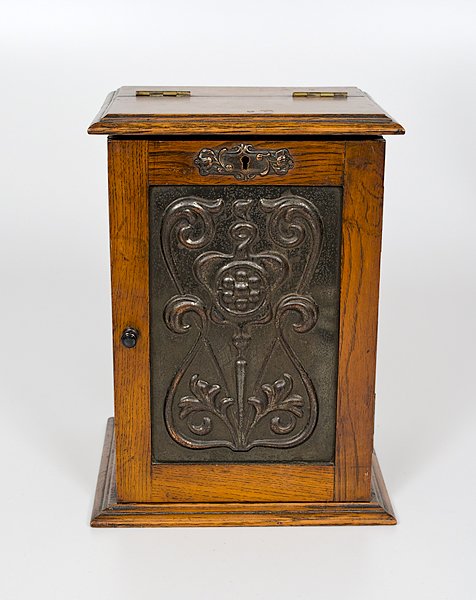 English Smoking Cabinet : England. A wooden smoking cabinet, the front door with copper tooled panel, the door and hinged top opening to reveal single drawer with a brass pull and a cutout for humidor and pipe holder; ht. 11.2