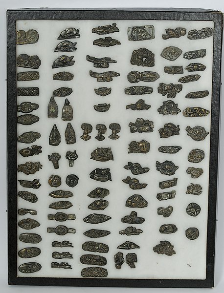 Japanese Menuki : Japan. An assembled group of ninety-four menuki in pressed tin, all of assorted forms, all unmarked; housed in a shadow box; largest lg. 1.75 in. Provenance:Private Collection, Vermont.