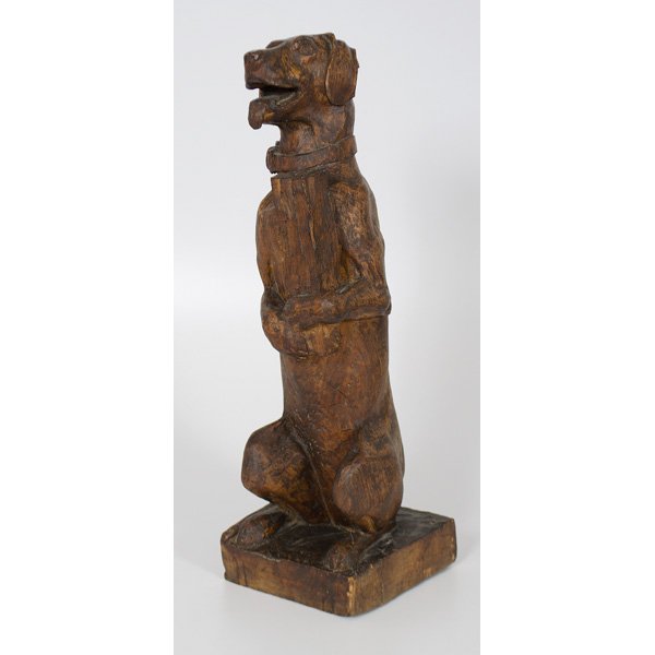 Carved Wooden Dog Sculpture : American. A folk art, carved wooden sculpture depicting a dog standing on its hind legs, wearing a collar and holding a log, unmarked; ht. 26.75 in.