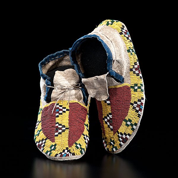 Sioux Beaded Hide Moccasins : sinew-sewn and beaded using colors of greasy yellow, rust, black, translucent green, marcasite, light blue, and white; cuffs edged in blue patterned cotton, length 10.5 in. late 19th century