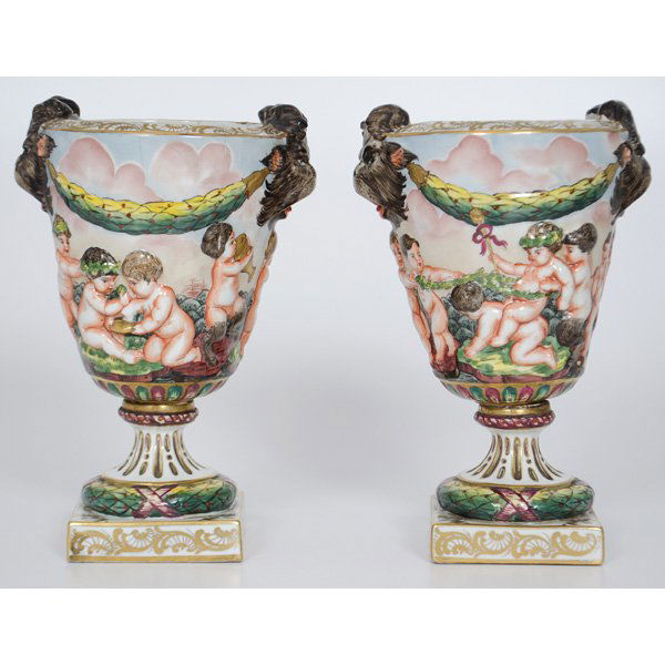 Capodimonte-Style Urns : French. A pair of Capodimonte-style urns with decorative beast-headed handles, the body having painted putti in relief within a processional scene with gilding, each with "N" and crown for Cap