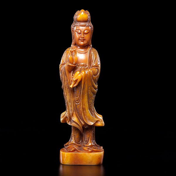 Chinese Soapstone: Guanyin: Chinese, 20th century. A butterscotch-colored soapstone carving of a standing Guanyin, wearing flowing robes with inscribed visvavajra designs, one hand holding a bottle, unmarked; ht. 10.5 in.