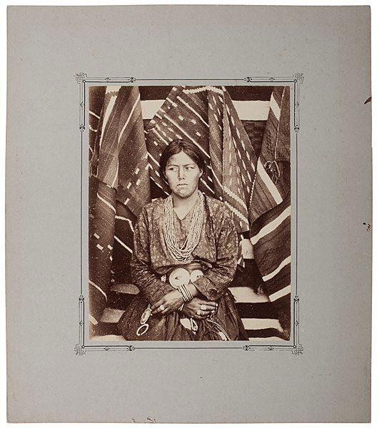 John K. Hillers Albumen Photograph, A Rich Navajoe : John K. Hillers Albumen Photograph, A Rich Navajoe Albumen photograph of an attractive, young Navajo woman wearing a large belt with metal medallions plus several pieces of jewelry, with rugs dra