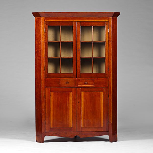 Cherry Corner Cupboard : American, 19th century. A cherry corner cupboard having a projecting cornice over two doors, each with glazed panels,over two center drawers, and two lower paneled doors; ht. 84, wd. 53, dp. 26 in.