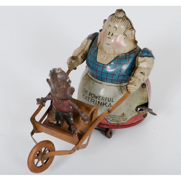 "The Powerful Katrinka" Tin Wind Up Toy : German, 20th century. Lithographed tin mechanical toy in the form of the character Katrinka, who pushes then lifts a wheelbarrow holding Jimmy when wound. Trademarked 1923 by Fontaine Fox; ht. 5.25 in