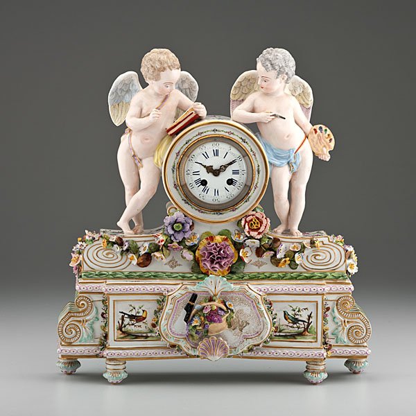 Meissen Porcelain Mantel Clock : German, late 19th century. A Meissen porcelain figural mantel clock with a gilt and polychrome enameled case with applied flowers, the dial flanked by putti depicting literature and art, the rectangul