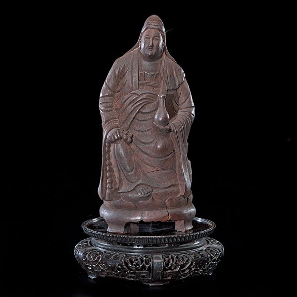 Chinese Bamboo Root Carved Buddhist Divinity Figure : Chinese, late 19th/early 20th century. A bamboo root carved Buddha figure holding prayer beads and a vase, on a carved rosewood stand; ht. of figure 9.75 in.