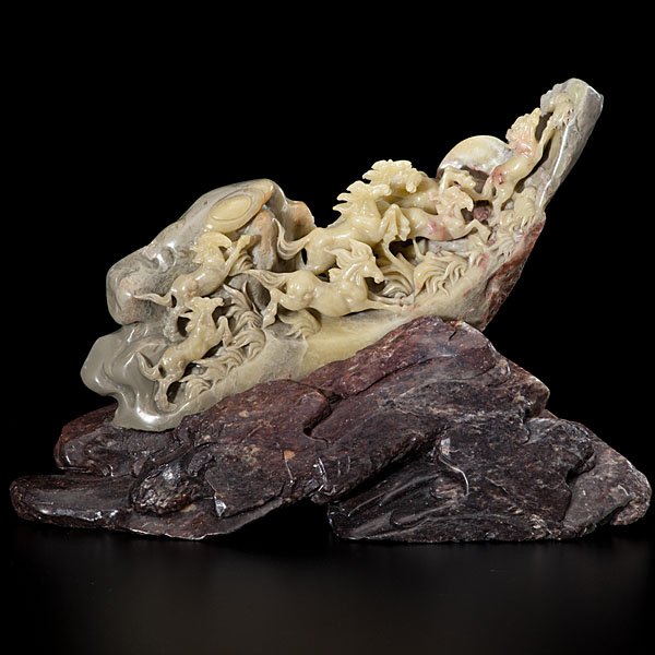 A Chinese Soapstone Mountain Carving with Galloping: Chinese, 20th century. A group of eight carved-jade horses galloping toward the precipice of a mountain through tall flowing grass, mounted on a grayish-brown soapstone base; ht. 7.5 in.