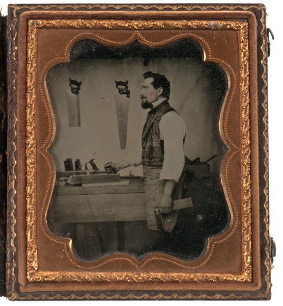 Occupational Sixth Plate Ambrotype of a Carpenter : Occupational Sixth Plate Ambrotype of a Carpenter Sixth plate ambrotype of a carpenter in profile, holding a square and planer, with mitre and panel saws visible hanging above his workbench. Hous