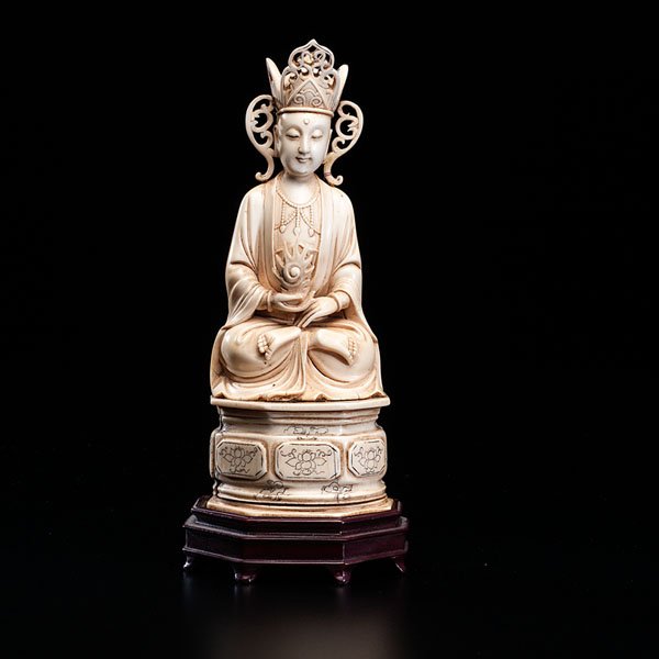 A Chinese Carved Ivory Buddha : A Chinese Carved Ivory Buddha 19th century. An inked ivory carving of a Buddha sitting on a throne, wearing a headdress and holding a torch, on a wood stand. Ht.: 9.5 in. Provenance: Private Col