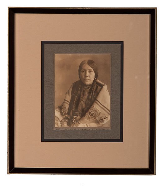 Richard Throssel Signed Photograph, Carries the War: Sepia toned platinum photograph of a young, Crow woman identified as Carries the War Staff, with blindstamped arrowhead and Richard Throssel's signature at lower right, copyright in negative lower 
