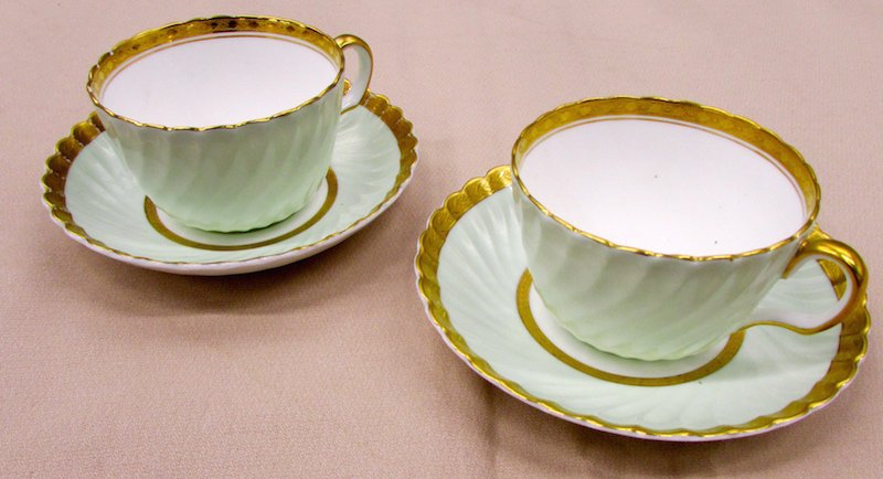 Two Mintons Cups and Saucers for Tiffany: Each in overall pale green with applied gold border with vine decoration, the undersides with Minton Crown over Globe marks and "Tiffany & Co.", the cups hand numbered "4905", the saucers "4987".