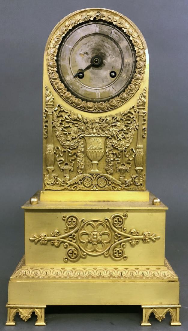 French Brass Clock with Relief Urn of Flowers: French brass clock, 19th c, decorated with relief urn of flowers, as found, 13 1/2"h x 7 1/2"w. W.A.I. does not guarantee clocks to be complete or in working condition.