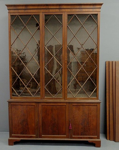 Mahogany two-part bookshelf cabinet with a dentil: Mahogany two-part bookshelf cabinet with a dentil molded cornice above cross-hatched glass doors over a lower section with crotch mahogany doors and shaped bracket feet. 87.5"h.x59"w.x17.5"d.