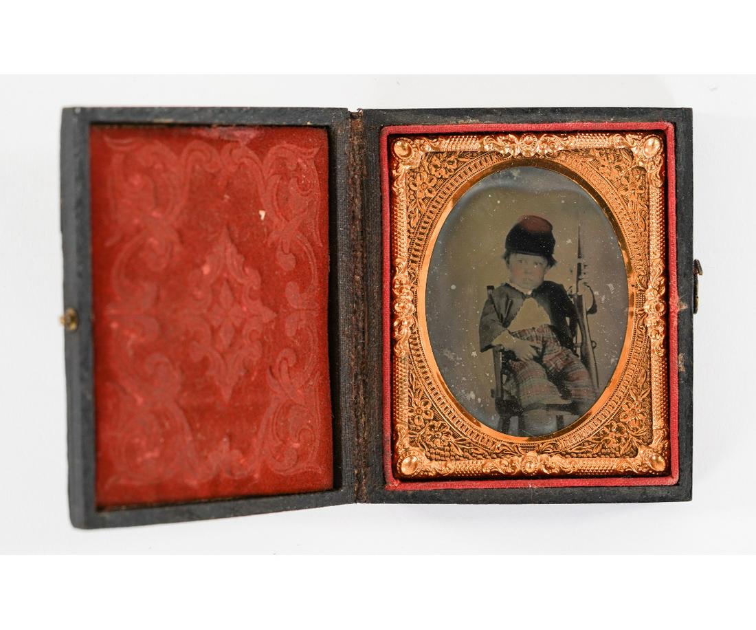 CIVIL WAR ERA AMBROTYPE: Civil War era ambrotype of a very young boy seated holding a gun and wearing a hat, mounted in a velvet lined period case. 3" x 2.25"