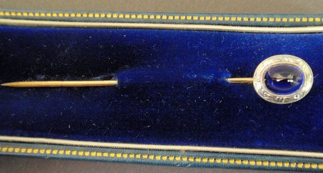 Bailey, Banks & Biddle sapphire stick pin, with a: Bailey, Banks & Biddle sapphire stick pin, with a platinum set blue sapphire cabochon, approximately 7.5mm x 6mm x 5.5mm, chase decorated platinum, 14k yg pin, #47831, 1.8dwt.