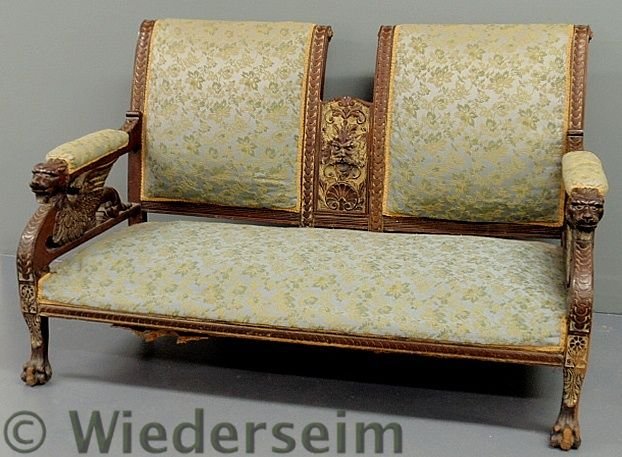 Victorian carved walnut settee, c.1890, with carv: Victorian carved walnut settee, c.1890, with carved winged griffin arm supports, grotesque face center back panel and paw feet. 37”h.x56”w.x26”d., seat 12”h.