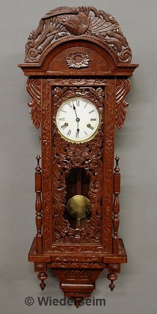 Carved German wall clock with a porcelain dial. 40: Carved German wall clock with a porcelain dial. 40"h.x13"w.