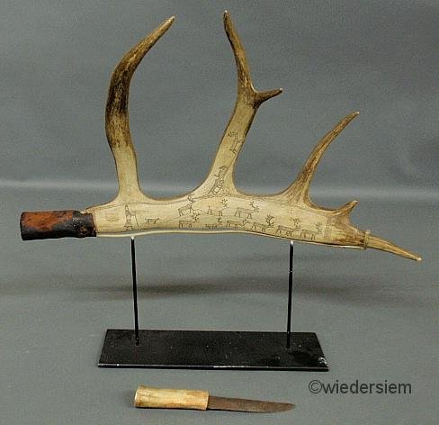 Rare Inuit reindeer horn carved and etched with a : Rare Inuit reindeer horn carved and etched with a scene with a herder, dog and reindeer, 19th c., the hollow end of the horn fitted as a sheath for a knife, and all mounted on a black metal stand. Ove