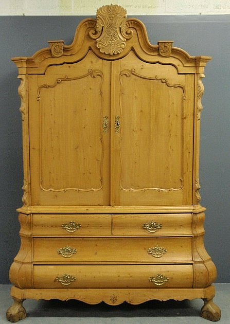 Continental pine two-piece cupboard, 19th c., with an o: Continental pine two-piece cupboard, 19th c., with an ornately carved cornice and a bombé base. 96”h.x60”w.x27”d.