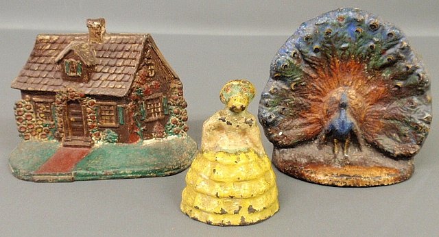 Three Victorian cast iron doorstops, log cabin, woman w: Three Victorian cast iron doorstops, log cabin, woman wearing a hop skirt and a peacock 7.5”h.x6.5”w.