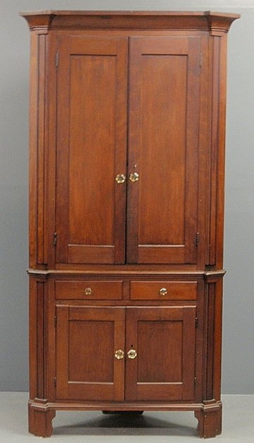 Walnut two-piece corner cupboard, c.1830, the top: Walnut two-piece corner cupboard, c.1830, the top section with an overhanging molded cornice above two blind paneled doors above a lower section with two drawers above two blind paneled doors and stra