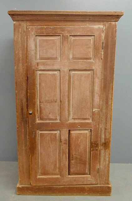 Pennsylvania German pine storage cabinet, c.1800, with: Pennsylvania German pine storage cabinet, c.1800, with a molded cornice above a raised panel door and molded base, and retaining the original red wash decoration. 67.75"h.x35"w.x19"d.