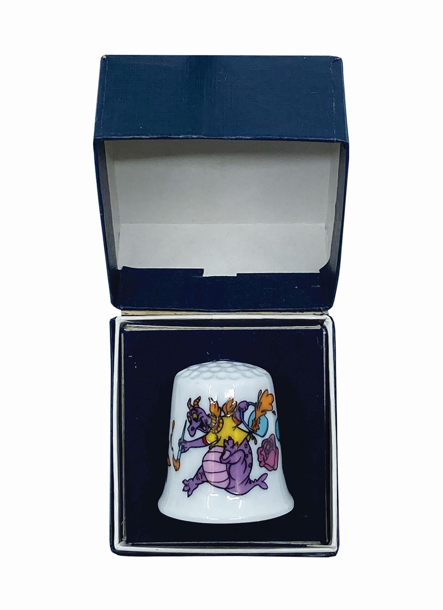 Journey Into Imagination Figment Ceramic Thimble.: (Epcot, 1982) A ceramic thimble featuring imagery of Figment painting flowers. The interior is marked with the Epcot logo. The thimble is still in its original box, which bears the original price tag 
