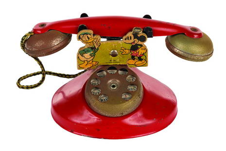 A Mickey & Donald Toy Telephone.: (N.N. Hill Brass Co., 1939) A red tin toy rotary telephone, decorated with Donald Duck and Mickey Mouse. Manufactured by the N.N. Hill Brass Co., a braided cord connects the headset to receiver, and t