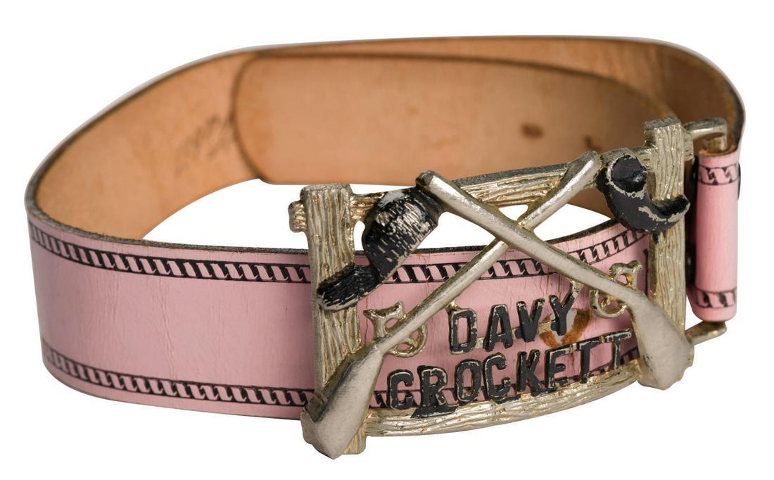 A Davy Crockett Belt by Fabil.: (Fabil, 1950s) A Davy Crockett Belt manufactured by Fabil. The pink and black belt is composed of hand-finished saddle cowhide and metal, marked size 26, and features Crockett's name, crossed rifles,