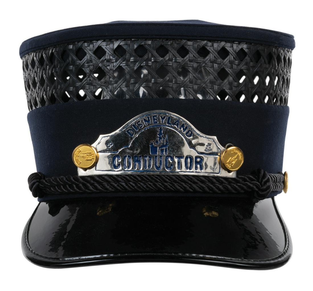 A Disneyland Railroad Hat & Conductor Badge.: (Disneyland, 1980s) A â€œDisney Double Decker” Hat & Conductor Hat Badge from the Disneyland Railroad. The navy-blue hat features a synthetic wicker and cloth textile crown, a black patent l