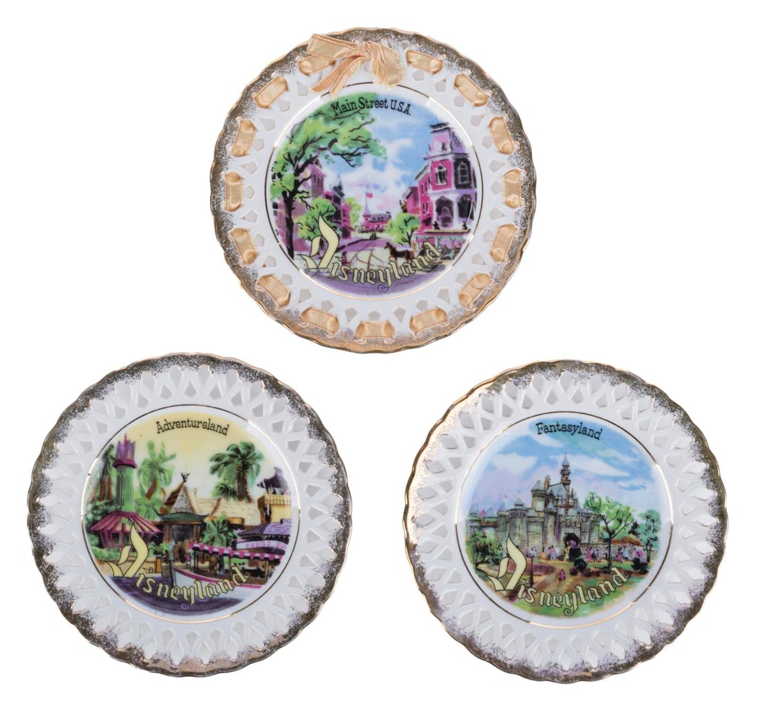A Set of Disneyland Souvenir Lace Plates.: (Disneyland, 1955-60s) A set of three ornate vintage Disneyland souvenir lace plates. The plates feature Main Street, Adventureland, and Fantasyland with colorful imagery, and are accented with gold-f