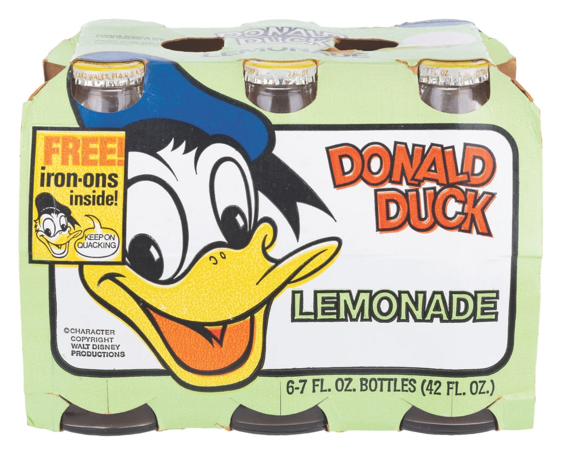 A Six Pack of Donald Duck Lemonade Bottles.: (Citrus World, 1970s) Six Donald Duck Lemonade 7-ounce bottles, with their original cardboard pack featuring an iron-on transfer. The bottles are unopened, containing the original beverage, and are in