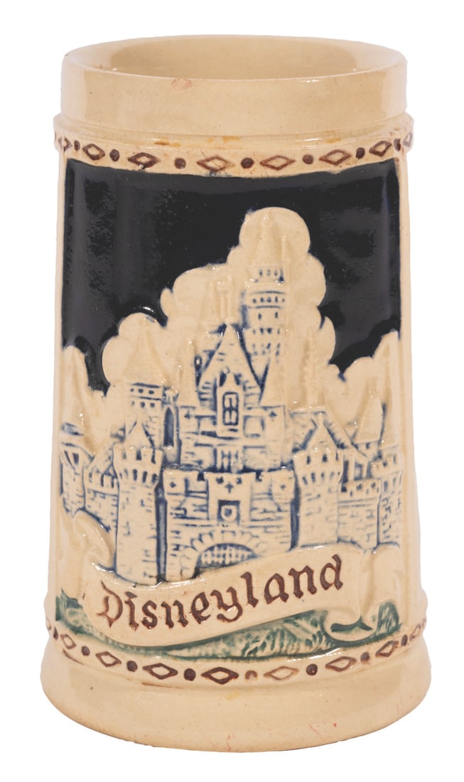A Disneyland Souvenir German Stein.: (Disneyland, 1956) A decorative souvenir ceramic stein featuring imagery of Sleeping Beauty Castle and icons representing the cardinal lands of Disneyland. This German-manufactured stein measures 3.25